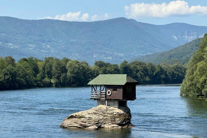 Wooden house on a rock in the Drina River with forested mountains in Western Serbia
