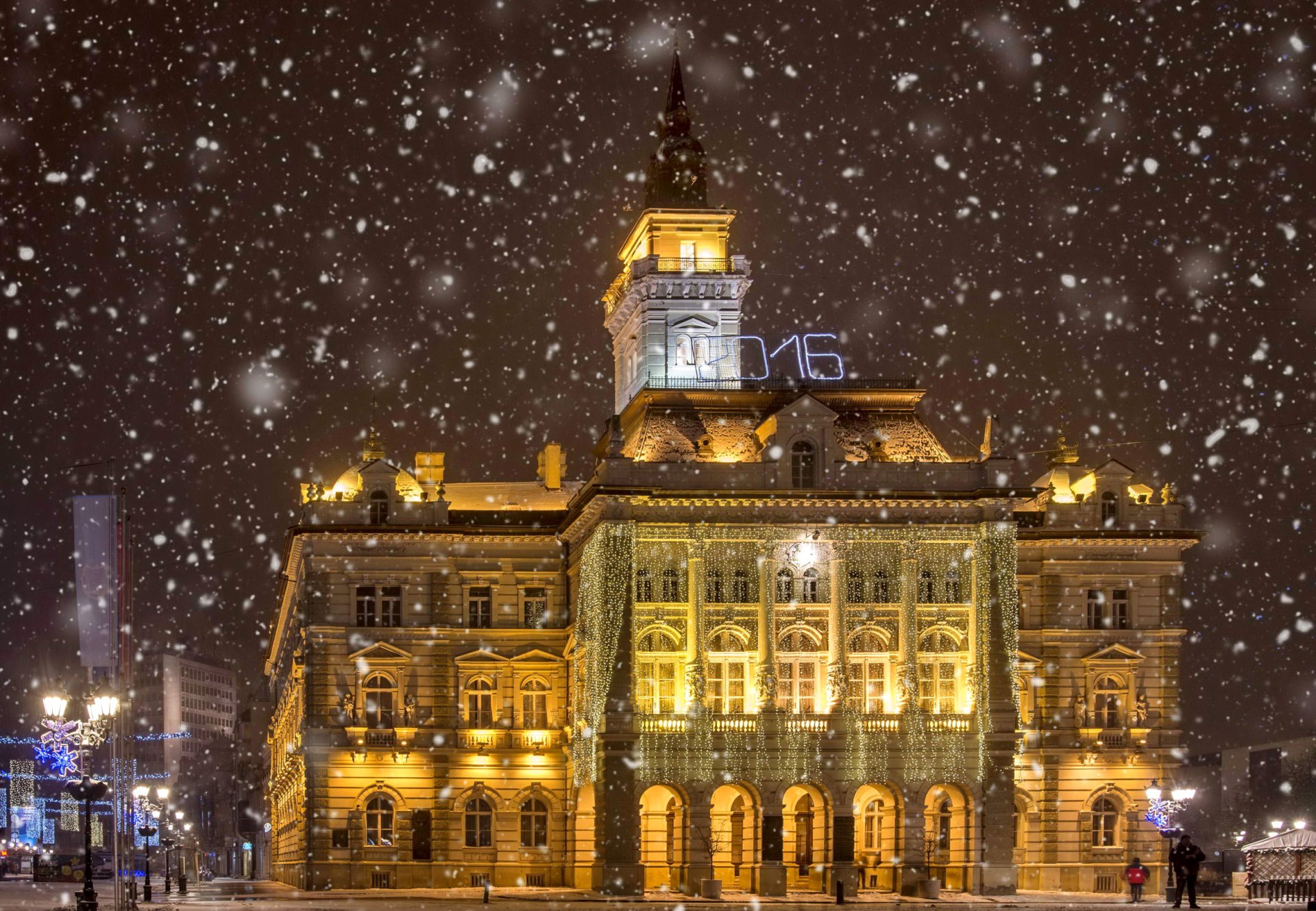 Illuminated Novi Sad city hall under falling snow at night