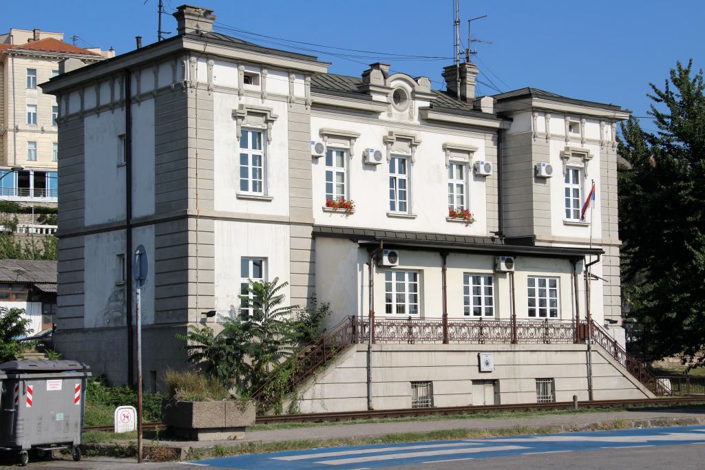 White historic building with ornate windows, balconies, and rail tracks in front in Belgrade