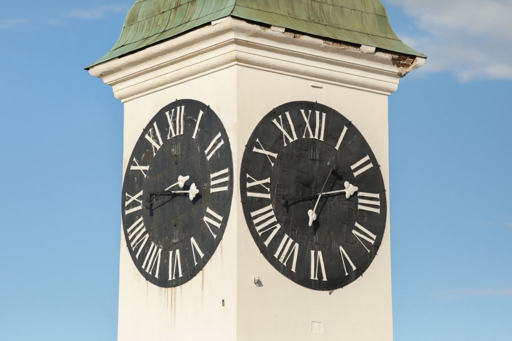 Twin black clock faces on the Petrovaradin Fortress tower beneath a green copper roof