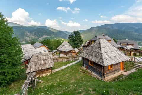 Wooden cottages on grassy slopes with mountains and clouds in Zlatibor