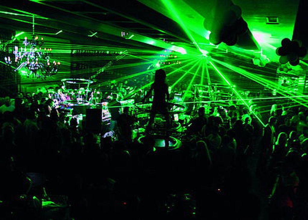 Crowded nightclub in Belgrade Nightlife with green laser beams and a DJ silhouette above the dance floor
