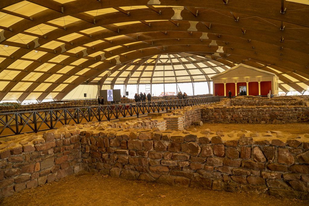 Stone ruins beneath a curved protective canopy at Mediana in Niš, with visitor walkways
